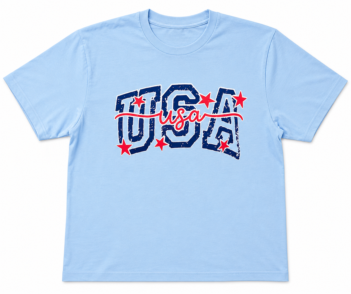 A light blue short-sleeve crewneck t-shirt featuring a distressed 'USA' graphic on the chest in navy blue with red stars and a red script 'USA' underneath.

