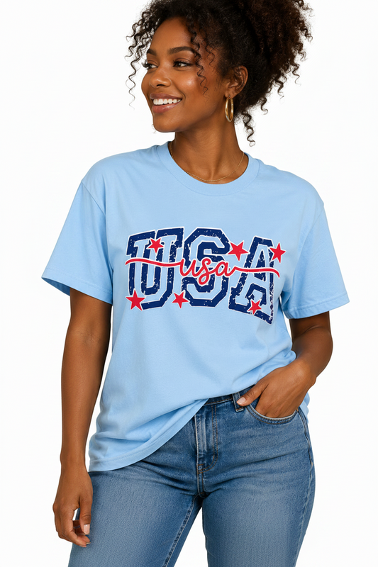 A woman wearing a light blue short-sleeve t-shirt with a 'USA' graphic in navy blue and red, paired with blue jeans, against a solid white background